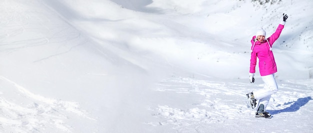 Banner of ski pistes and white mountain with young woman in pink ski jacket, white gloves, hat and ski boots on the right, bending her knee and holding one hand up on a sunny day.