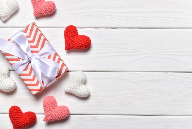 A banner for Valentine's Day with knitted hearts in a row on the right side on a white wooden background. February 14.