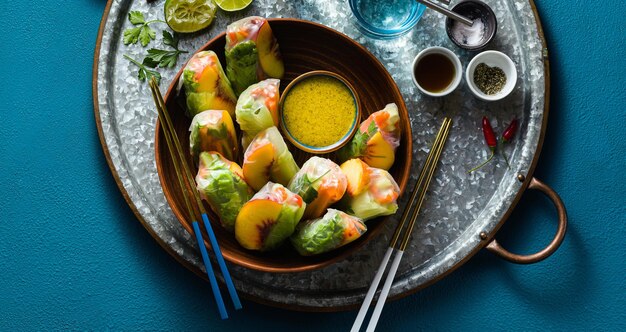 Banner di involtini primavera vegani di verdure e pesca con salsa di pistacchio su un vassoio cibo sano girato dall'alto spazio di copia