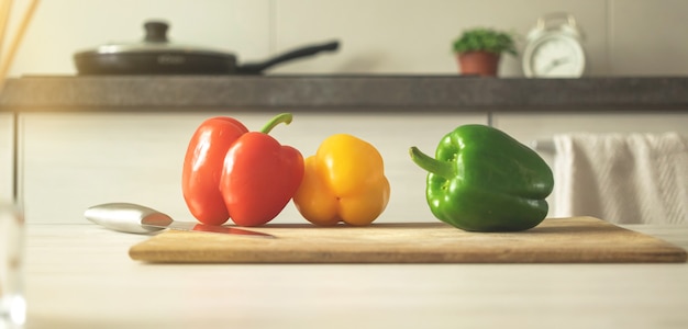 モダンなキッチンの背景に赤、黄、緑のピーマンとまな板のバナー。野菜の食材、健康食品のコンセプト写真を調理