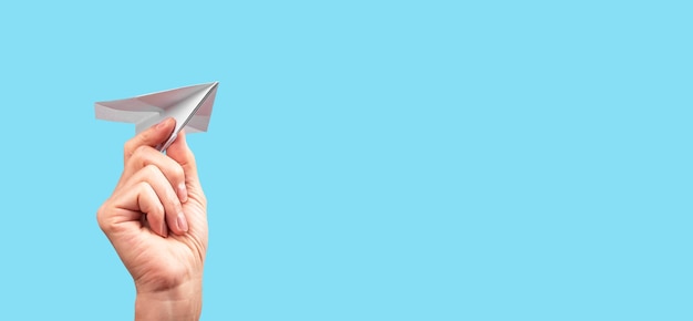 Foto banner con mano femminile che lancia aereo origami su sfondo turchese aeroplano di carta fatto a mano concetto di divertimento per l'infanzia della libertà luogo per il testo