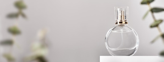 白い表彰台にガラスの香水瓶が付いたバナー花のユーカリの配置最小限のモックアップスタイルのソフトフォーカス