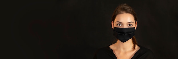 Banner with a young brunette girl in face mask on dark background.