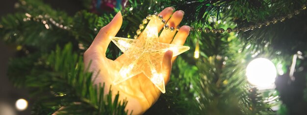 Foto banner delle mani della donna che decorano luci e ornamenti albero di natale per celebrare la stagione invernale e di dicembre