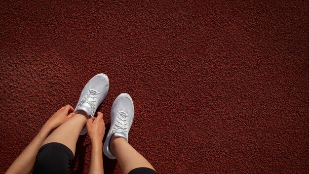 Banner women's legs. A woman's hand tying the laces on her sneakers at the stadium. Preparing to run. Space for text. Top view. Vertical