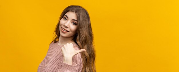 Banner a young woman in a sweater stands on a yellow background and points her finger to the side mockup