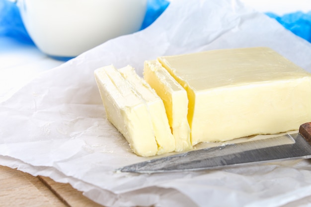 A bar of butter on a wooden board with a knife, on a white table. Ingredients for cooking.