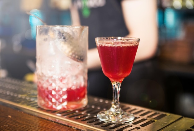 On the bar counter there is a mixing glass with the remnants of\
a cocktail and a readymade cocktail in a glass horizontal\
photo