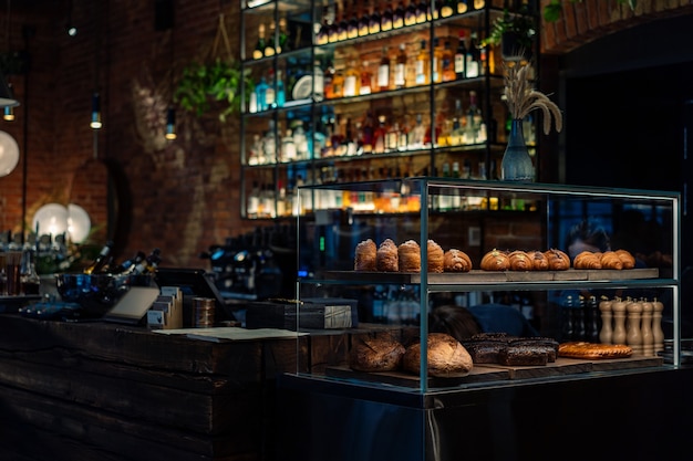 Bar counter with a pastry showcase in small restaurant Bottles Of Alcohol And Spirits On Backlight