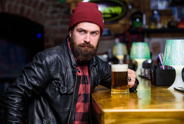 Bar is relaxing place to have drink and relax Hipster relaxing at bar Man with beard spend leisure in dark bar Brutal lonely hipster Friday evening Brutal hipster bearded man sit at bar counter