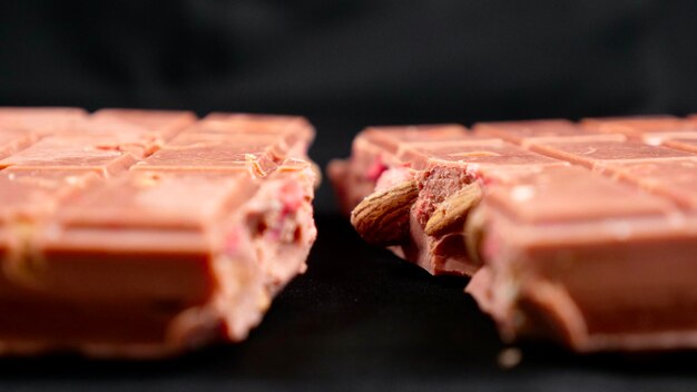 Photo a bar of pink ruby chocolate with freezedried strawberries and almonds closeup isolated black