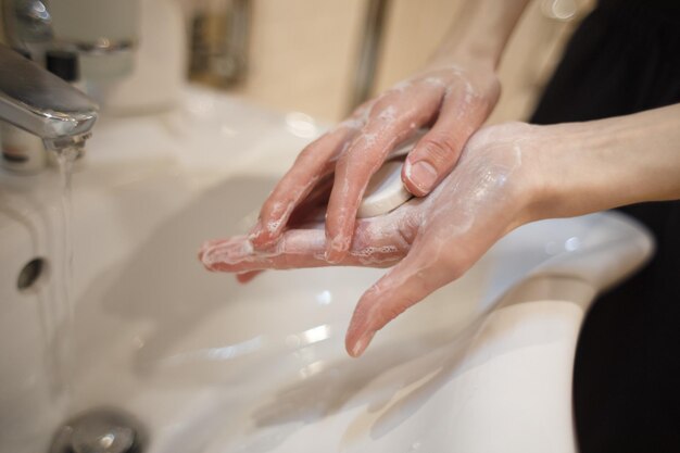 A bar of soap in soapy hands near the water tap in the sink