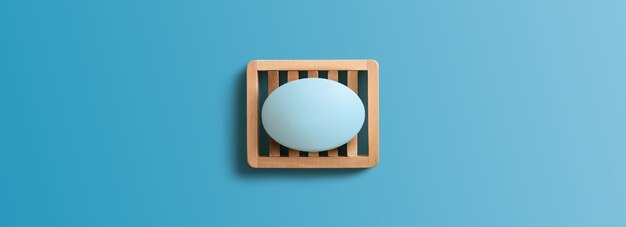 Bar of soap in wooden dish on blue background. Directly above, Copy space.