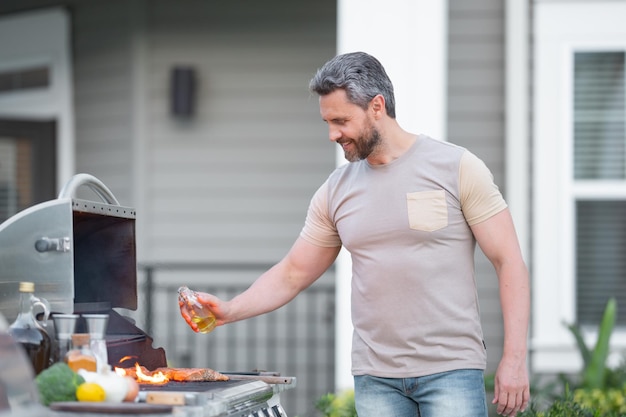 Barbecue concept Spaanse man van middelbare leeftijd in t-shirt voor het roosteren en grillen van voedsel op de barbecue