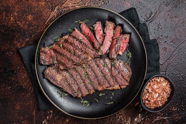 Barbecue denver strip beef meat steak on a plate Dark background Top view