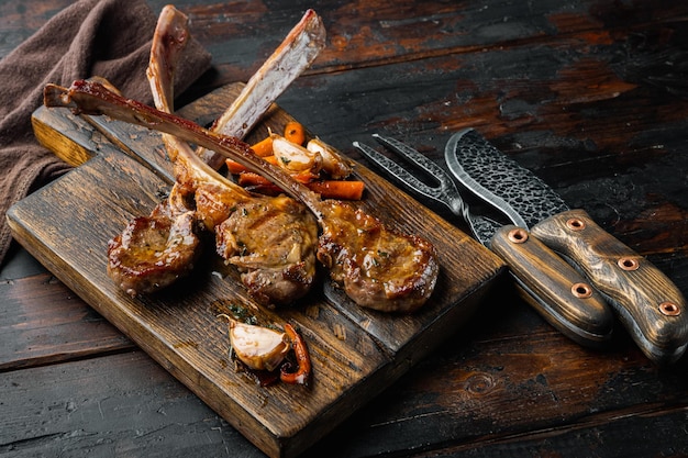 Photo barbecue dinner. grilled lamb meat chops with onion and thyme set, on wooden serving board, on old dark  wooden table background