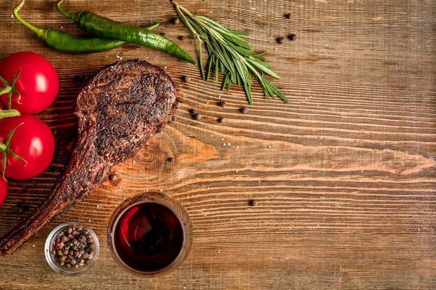 Barbecue dry aged rib of beef with vegetables and glass of red wine close-up on wooden background. Top view. Copy space. Still life. Flat lay