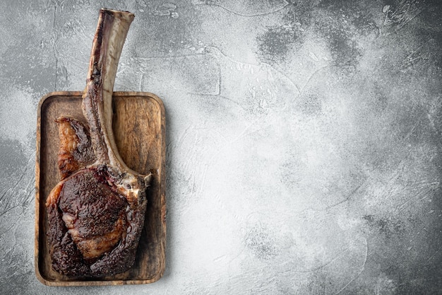 Barbecue dry aged Tomahawk Steak beef meat set on wooden serving board on gray stone background top view flat lay with copy space for text