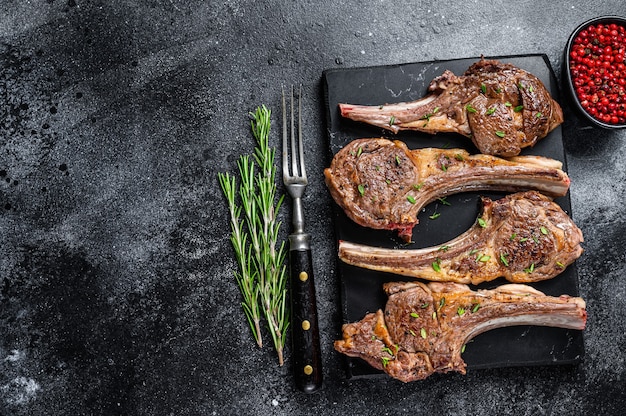 Barbecue fried lamb meat chops on a marble board. Black background. Top view. Copy space.