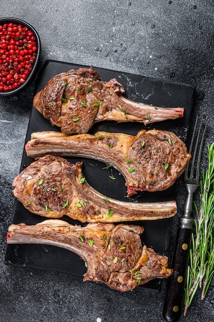 Barbecue fried lamb meat chops on a marble board. Black background. Top view.