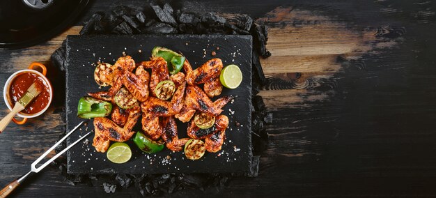 Barbecue gebakken kippenvleugels op een stenen dienblad liggend met een vleesvork.