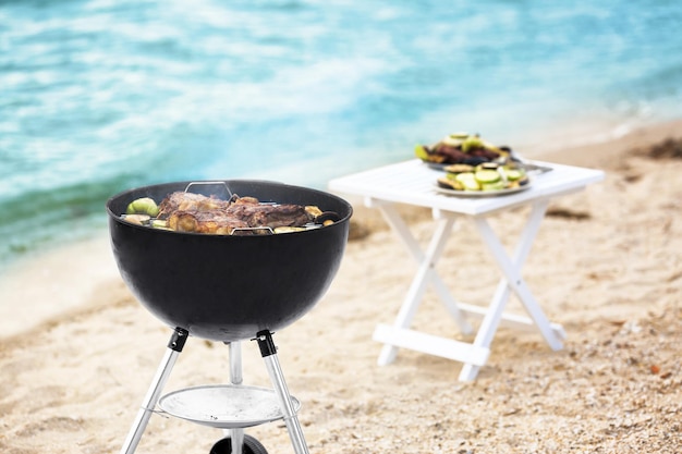 Barbecue grill with tasty steaks and vegetables on beach