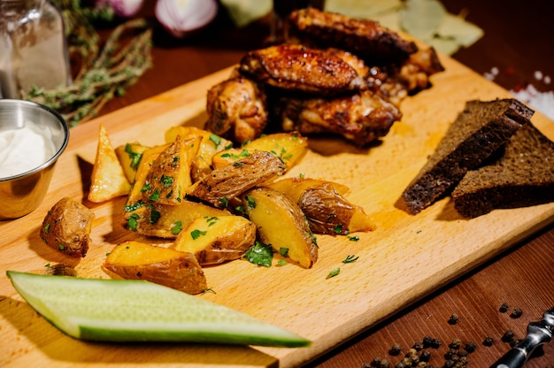Жареные на гриле куриные крылышки заделывают с картофелем фри, соус на деревянных фоне. Концепция мясной пищи.