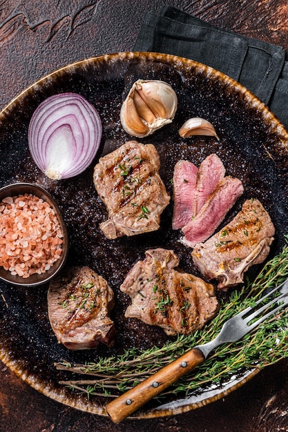 Barbecue Grilled lamb loin chops steaks saddle in a plate with herbs Dark background Top view