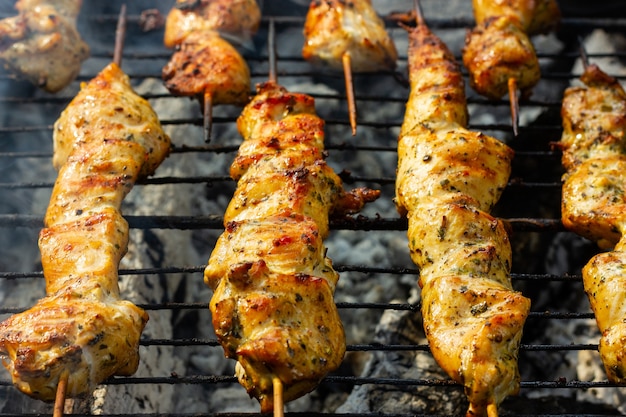 Barbecue meat on wooden skewers on the grill grates against the background of smoke and hot coals ch...