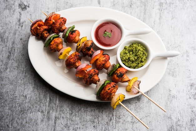 Barbecue of tandoori Mushroom Tikka, geserveerd in een bord met groene chutney en ketchup. selectieve focus