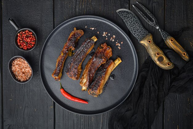 Barbecue pork spare ribs with fruit relish set, on plate, with barbeque knife and meat fork, on black wooden table table, top view flat lay