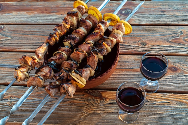 Barbecue prepared on grill and glasses of red wine, on wooden table.