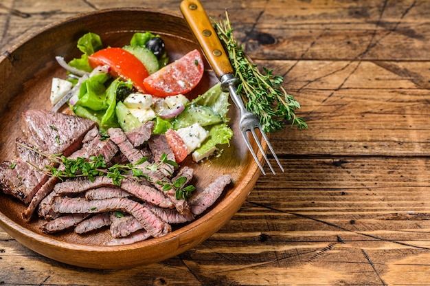 Barbecue rundvlees karbonade rumpsteak op een houten plaat met groentesalade. houten achtergrond. bovenaanzicht. ruimte kopiëren.