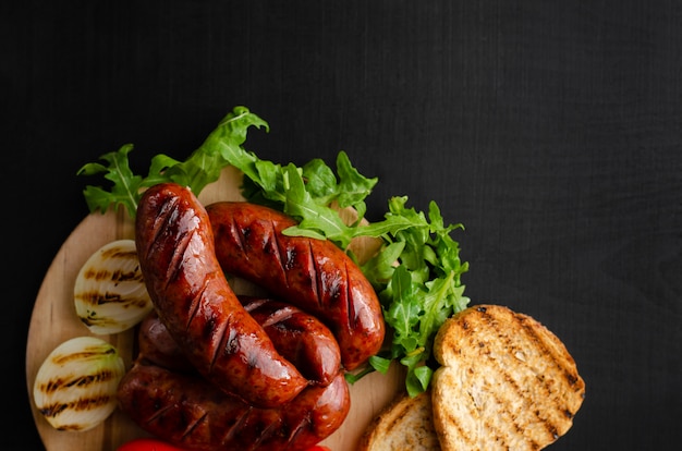 Salsicce barbecue, pane tostato, cipolla e rucola fresca su sfondo nero. , disteso