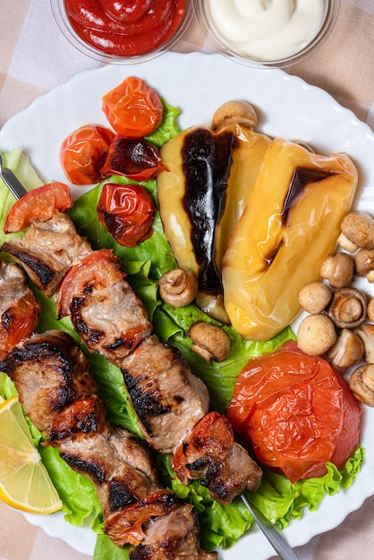 Barbecue on skewers with lettuce and baked vegetables on a white plate