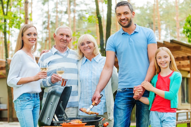 Barbecue tijd. Gelukkig gezin van vijf mensen die vlees barbecueën op de grill en naar de camera kijken