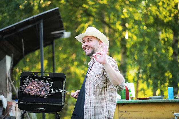 Barbecue time. European man in hat waiting for grilled food. He is sitting near fire and rest.