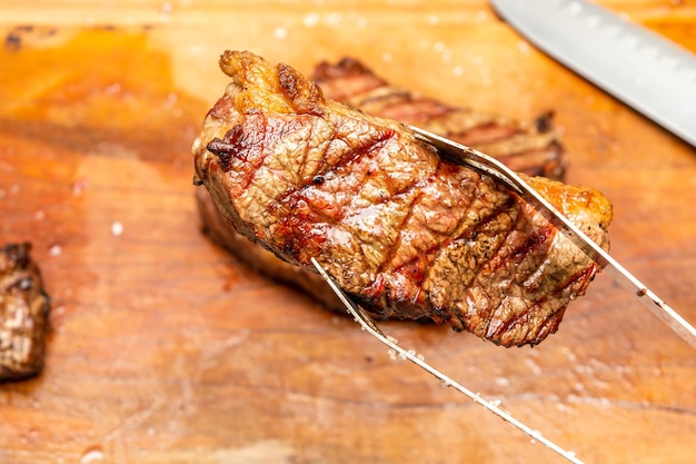barbecue tongs hold picanha steak on a barbecue party background