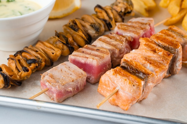 Barbecue zeevruchten kebab met gegrilde mosselen, tonijn, zalm op een houten spies met witte saus en citroen.