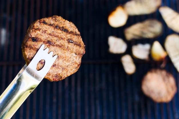 Barbecued meat cutlet in forceps during picnic