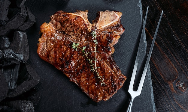 Barbecuesteak op een zwarte leisteen bord met vlees vork en grill kolen