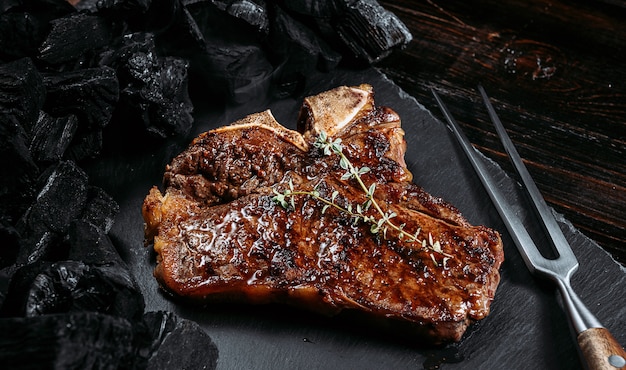 Barbecuesteak op een zwarte leisteen bord met vlees vork en grill kolen