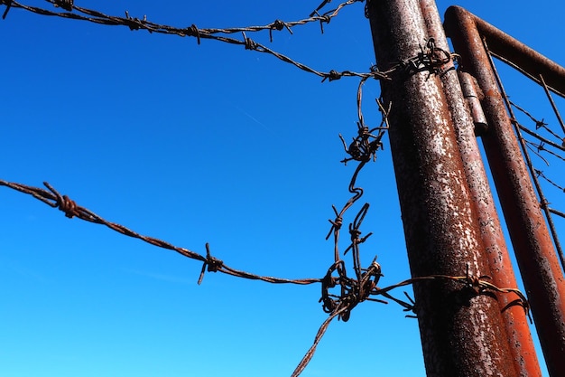 Barbed wire double wire metal tape with sharp spikes for barriers Rusty barbed wire against the blue sky The concept of war restriction of rights and freedoms Iron pole