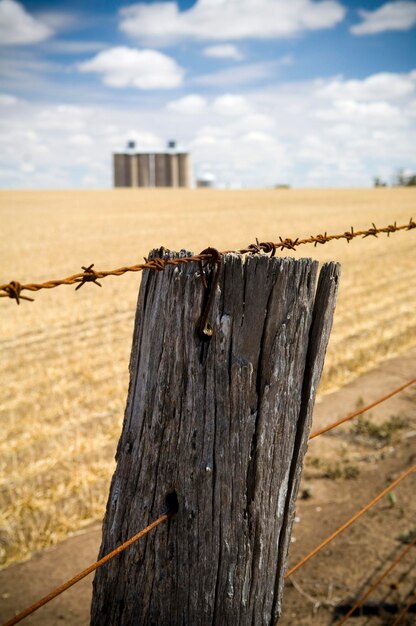 Barbed wire fence on wooden post against sky