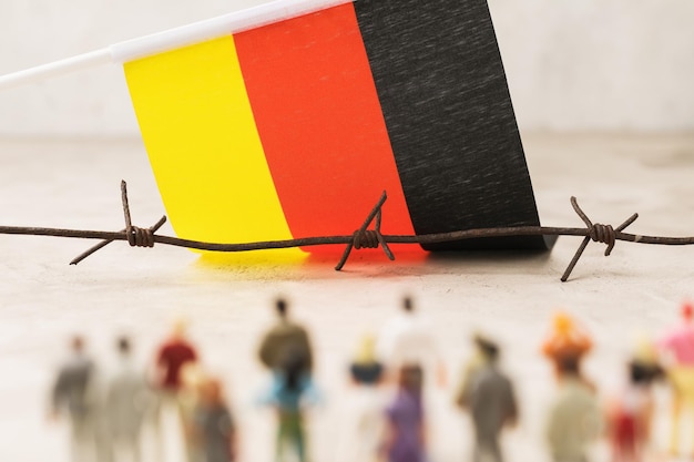 Barbed wire flag of Germany and plastic toy men concept of illegal border crossing by migrants