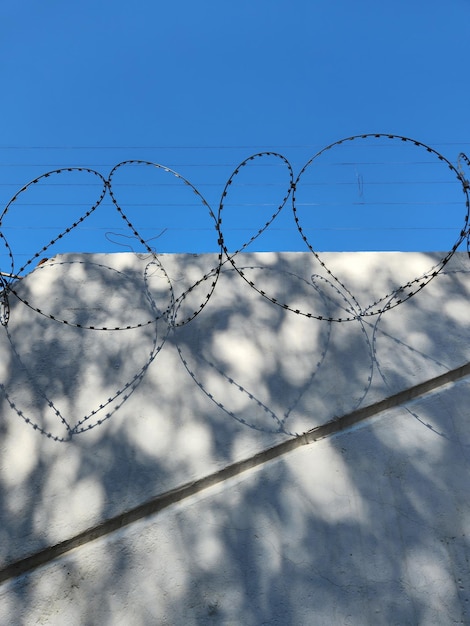 Barbed wire on white wall and blue sky with shadows from bright sun