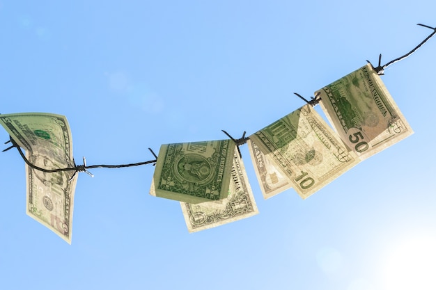 Barbed wire with american dollars bills against blue sky