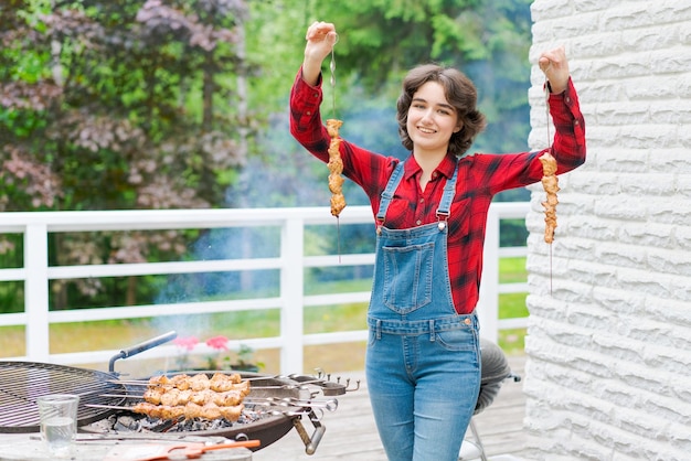 デニムのオーバーオールと赤い格子縞のシャツを着た若い女性と庭でバーベキュー パーティー