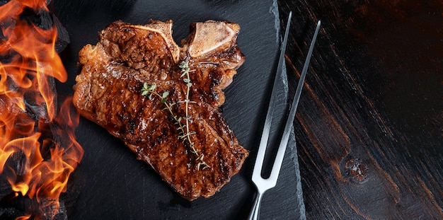 Barbeque steak on a black slate board with meat fork and grill coals