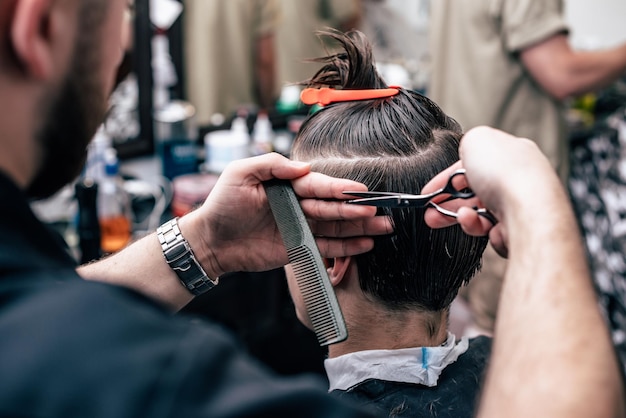 Barbiere in barbershop taglio auto elettrica per capelli a giovane ragazzo hipper per acconciatura alla moda.